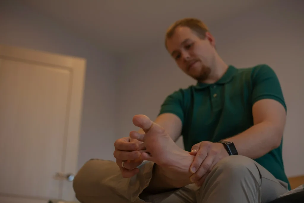 An image of a man sitting and holding his foot, appearing to examine or massage it, possibly due to discomfort or pain associated with neuropathy.