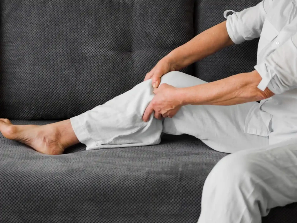 A person sitting on a gray couch, holding their leg in discomfort.