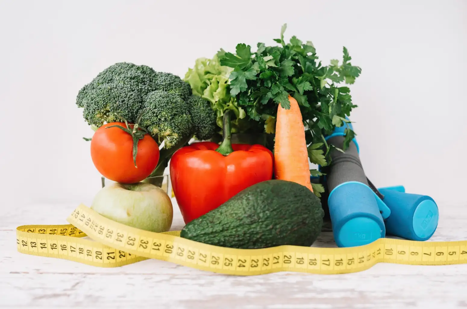 A collection of fresh vegetables, fruits, and dumbbells with a yellow measuring tape, symbolizing healthy eating, fitness, and weight management.