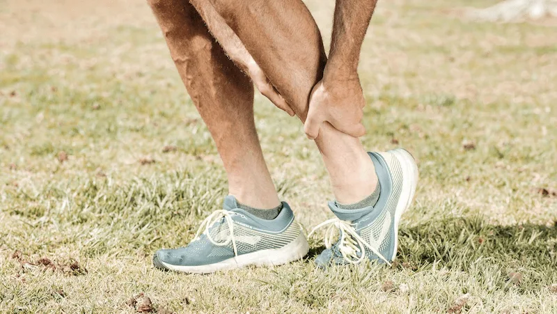 Close-up of a person holding their ankle in pain, representing neuropathy-related ankle discomfort.
