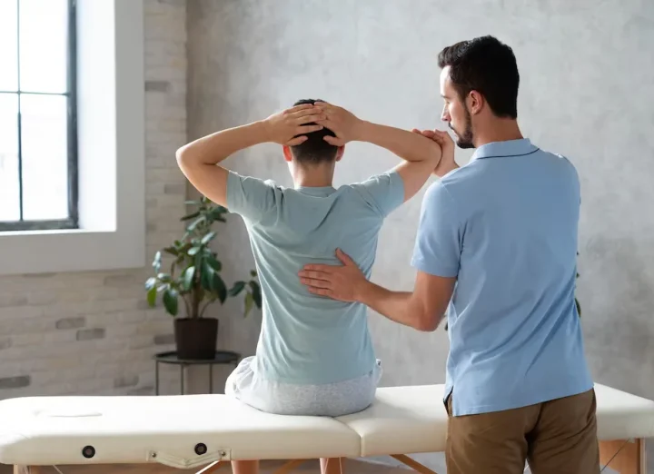 Physical therapist assisting a male patient with back and shoulder exercises during a rehabilitation session.